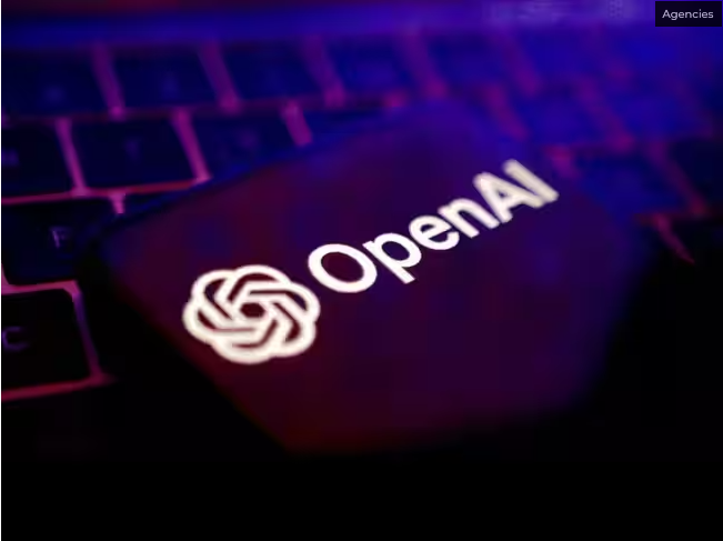 보라색과 분홍색 조명이 비치는 노트북 키보드 위에 흰색 오픈AI(OpenAI) 로고와 영문 표기가 적힌 어두운 물체가 놓여 있고 오른쪽 상단에 'Agencies' 라벨이 표시되어 있다.